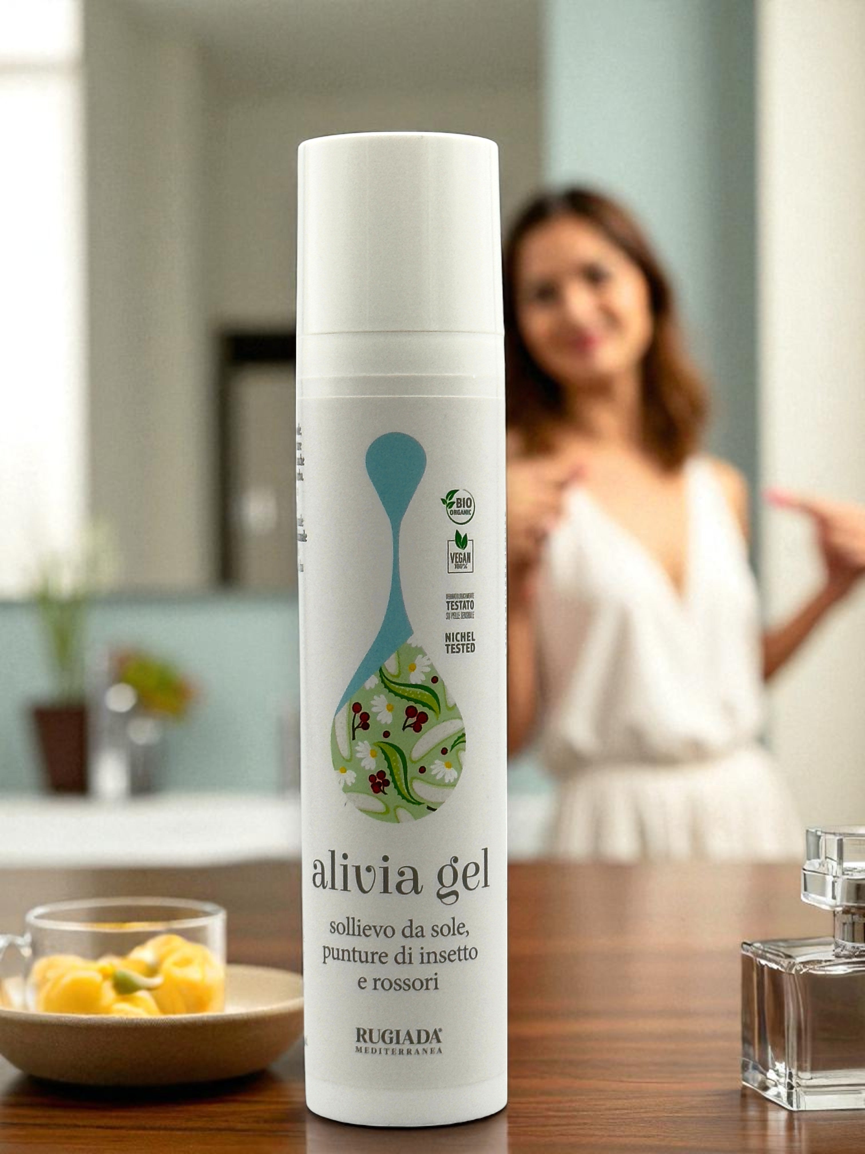 Flacone di Alivia Gel su tavolo con donna sorridente sullo sfondo, simboli di valori visibili sull'etichetta.
